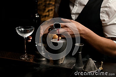 Close-up male bartender pours drink from metal jigger into steel cup of shaker Stock Photo