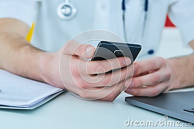 Close up male doctor or medical student using mobile smart phone working on laptop computer in hospital. Stock Photo