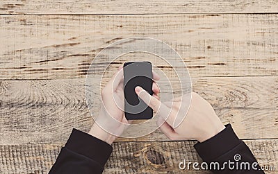 Close up of male hands holding smartphone and pointing finger to graph and text on screen at table wooden planks. Hipster style. T Stock Photo