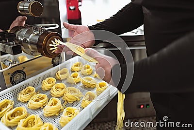 Close up male hands preparing fresh fettucine using machine in pasta factory Stock Photo