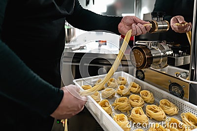 Close up male hands preparing fresh fettucine using machine in pasta factory Stock Photo