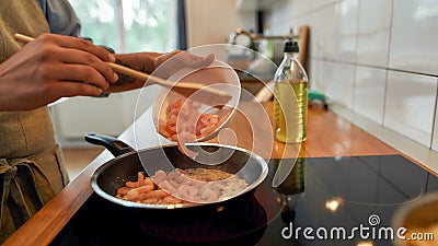 Close up of man adding shrimp to sauteed garlic and onion in the frying pan. Cook preparing dish with seafood Stock Photo