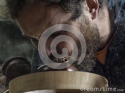 Close-up A man with a beard breathes smoke into a traditional teapot made of yixing clay. brown pottery teapot Stock Photo