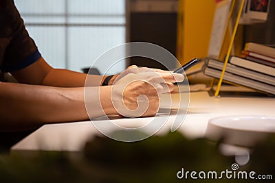 Close up man hand holding mobile phone. Business man typing on smart phone on office desk with books in background Stock Photo