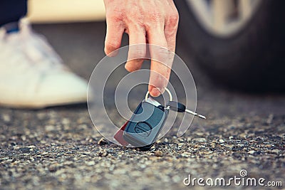 Close up of man hand lifting car keys fallen on the ground. Guy found vehicle keys someone lost on the asphalt road in the parking Stock Photo