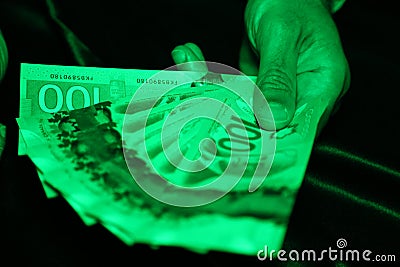 A close up of a man`s hands holding Canadian money under a green light- $100 bill Stock Photo