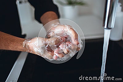 Close up of man`s hands in soap foam. Washing fingers and palms and cleaning them. Water pouring out of tap into sink in Stock Photo