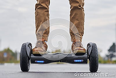 Close up of man using hoverboard on asphalt road. Feet on electrical scooter outdoor, front view Stock Photo