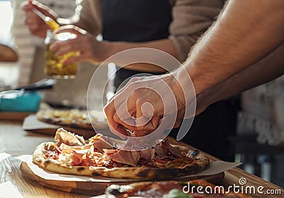 Close-up of a man and a woman& x27;s hands are preparing pizza in the kitchen in a restaurant, laying out the meat and oiling Stock Photo