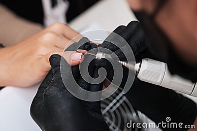 A close-up of a manicure master processing the nail surface with a cutter on an electric machine, removing burrs. The concept of a Stock Photo