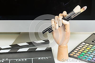 Close-up of mannequin hand with makeup bushes, colorful makeup palette, clapboard on table Stock Photo