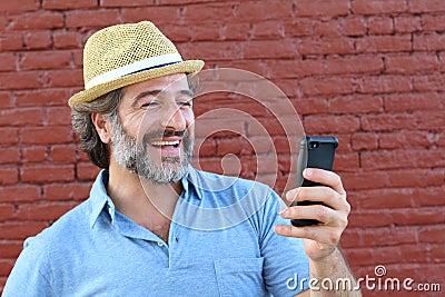 Close up of a mature man leaning against a red wall using mobile phone. Portrait of a happy business man holding a smartphone Stock Photo