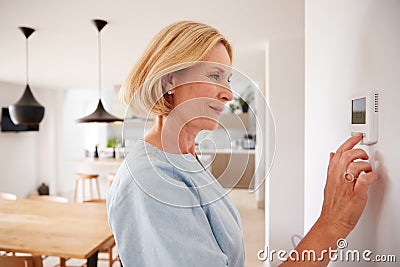 Close Up Of Mature Woman Adjusting Central Heating Temperature At Home On Thermostat Stock Photo