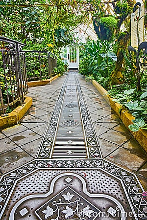 Close up of metal grating on tile walkway inside conservatory with plants on sides of walkway Editorial Stock Photo