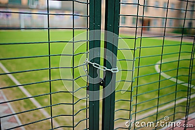 Close up metallic net-shaped green fence that closed and wrapped by chain on a background of school football field Stock Photo