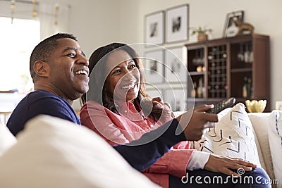 Close up of middle aged couple sitting on the sofa in their living room using remote and watching TV, laughing, close up Stock Photo