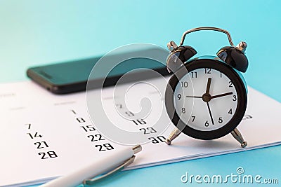 Close up of mini alarm clock, calendar and white pen and smartphone on blue background. Business meeting planning, deadline Stock Photo