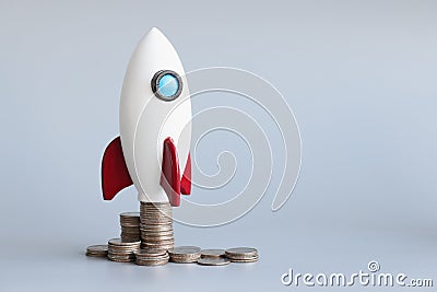 Miniature rocket stand on stack of coins, rocketship as symbol to open business project Stock Photo