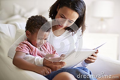 Close up of African American young adult mother sitting in an armchair reading a book with her three year old son on her knee, la Stock Photo