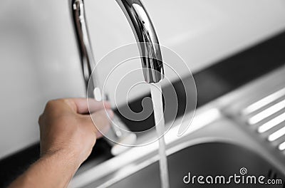 Male hand and close up on modern kitchen metal faucet and metal kitchen sink with a running water. Stock Photo
