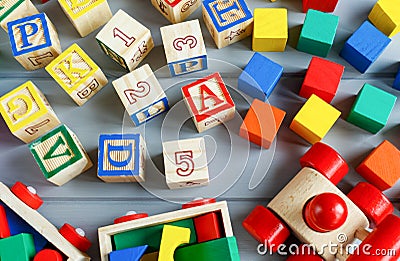 Close up Multicolored wooden cubes with letters, car, rainbow arc on gray background. Set of toys for studying alphabet. Education Stock Photo