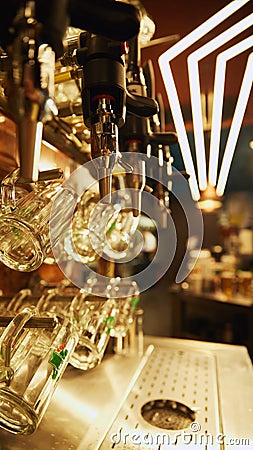 Close-up of multiple shiny beer taps with handless, set against blurred background with rows of empty glasses and bar Stock Photo