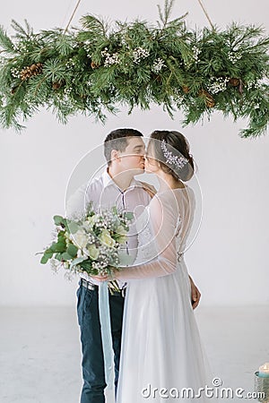 Close up of a nice young wedding couple. Wedding ceremony in light white room decorated with pine, flowers and candles. Stock Photo
