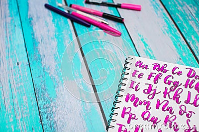 Close up of notebook with hand drawn abc alphabet letters and colorful pens on blue wooden desk background Stock Photo