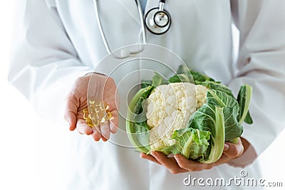 Young nutritionist holding omega pills in one hand and cauliflow in the other hand over white background. Stock Photo