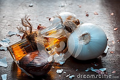 Close up of oil of onion or Allium cepa L oil on a wooden surface with raw onions in dark Gothic colors.This oil Cures Fever,Nouri Stock Photo