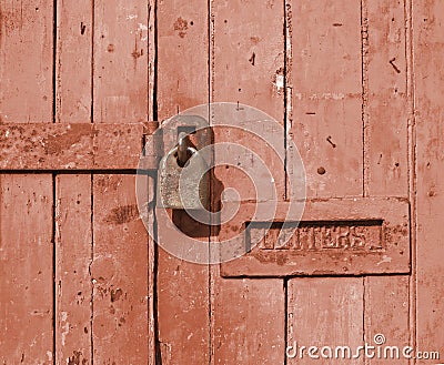 Close up of an old brown wooden door with faded paint and a rusty closed padlock and old metal letterbox Stock Photo