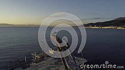 Close-up of old and destroyed ship trunk and gull sitting on a rusty pipe against the sunset sky. Shot. Marine Stock Photo