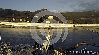 Close-up of old and destroyed ship trunk and gull sitting on a rusty pipe against the sunset sky. Shot. Marine Stock Photo