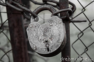 A close-up of an old locked iron lock with traces of paint on a thick chain wrapped between the gates of a metal fence on a gray Stock Photo