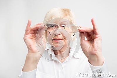 Close up of old woman is very attentive to details. She is looking to her glasses trying to find dirty spots there. She Stock Photo