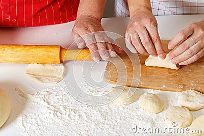 Close-up. The older woman in the red kitchen apron rolls out the dough with a rolling pin, the adult daughter sculpts cakes Stock Photo