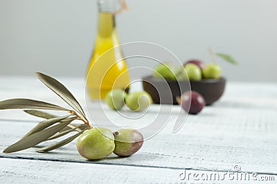 Close up olive branch glass bottle of olive oil and wooden breakfast bowl with raw turkish olive seeds and leaves on white rusti Stock Photo