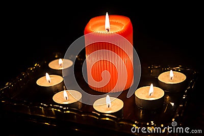 Close up of one big and six small burning candles on a dark desk Stock Photo