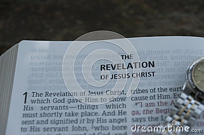 Close-up of open Bible in Revelation of Jesus Christ in chapter 1 with clock. Copy space. Stock Photo