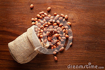 Close-up of organic red-brown peanuts Arachis hypogaea spilled out from a laying jute bag over wooden brown background Stock Photo