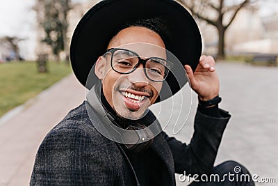 Close-up outdoor portrait of excited young man with brown skin wears glasses. African bearded boy in hat expressing Stock Photo