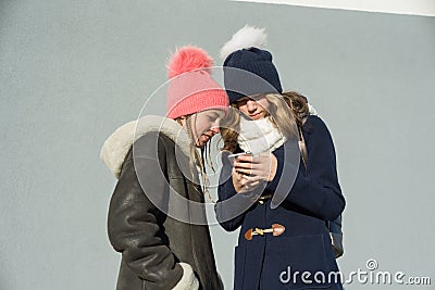 Close-up outdoor winter portrait of two teenage girls students in profile smiling and talking, girls looking at mobile phone Stock Photo