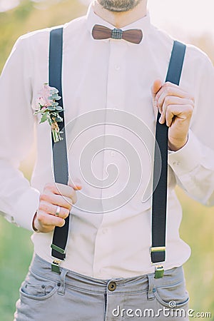 The close-up outlook of the groom in the white shirt, gray pants, suspenders with the flower accessories and wooden Stock Photo