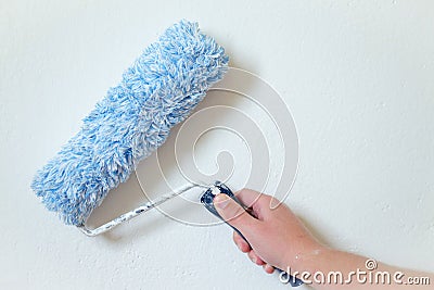 Close up of painter arm painting a wall with paint roller. Professional Workman Hand holding Dirty Paint roller. Stock Photo