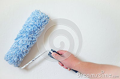 Close up of painter arm painting a wall with paint roller. Professional Workman Hand holding Dirty Paint roller. Stock Photo