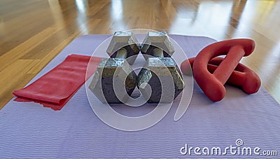 Close up of a pair of dumbbells, theraband exercise bands, and a yoga mat on hardwood floor Stock Photo