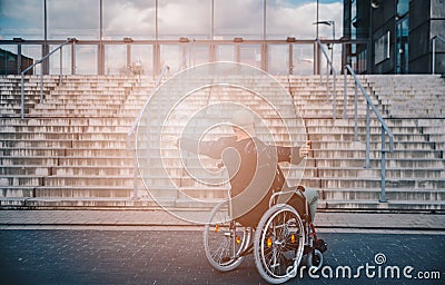 Paralyed man sitting on wheel chairin front of the stairs with raise arms. Stock Photo