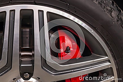 Close-up on a part of an aluminum wheel through the spokes of which a perforated brake disc and a red support of a sports car are Stock Photo