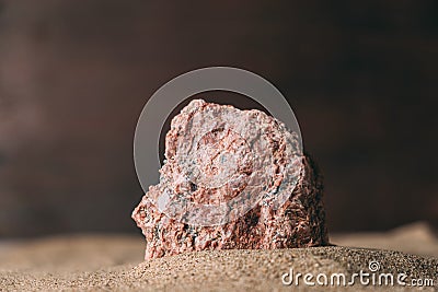 Close-up of part of pink stone sticking out of sand against dark background. Stock Photo