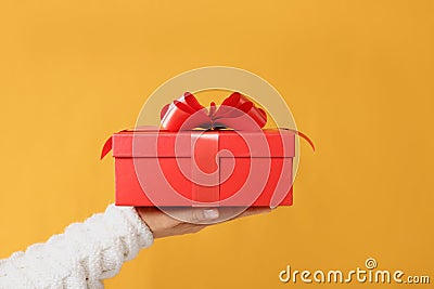 Close-up partial view of man in sweater holding red gift box on yellow background.Gift giving concept Stock Photo